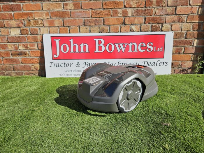 "Husqvarna Automower® 310E NERA robotic lawn mower operating on a well-maintained lawn. The compact, modern mower is navigating near the lawn's edge, showcasing its EdgeCut precision and sleek design. Ideal for gardens up to 1000m², the mower offers smart features like wireless installation, zone control, and remote app connectivity.