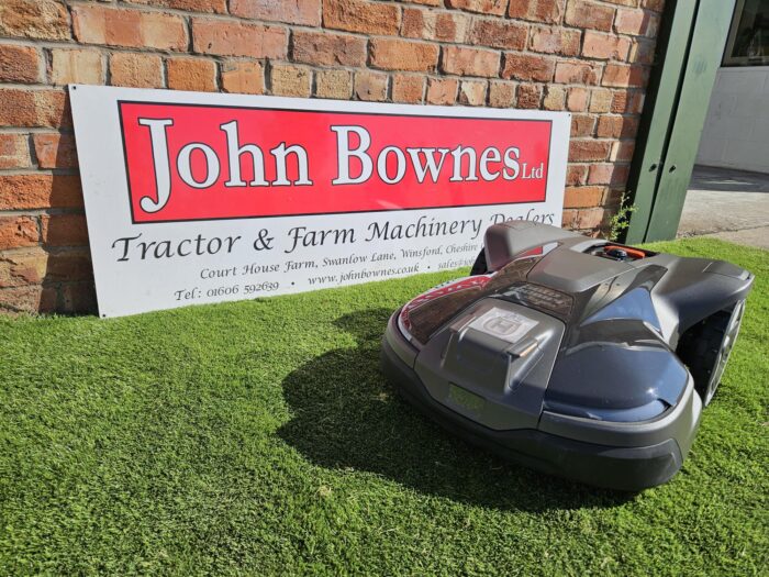 Husqvarna Automower® 450X NERA robotic lawn mower working on a large, sloped lawn with dense grass and landscaping. The mower is shown navigating rough terrain, highlighting its durable design, obstacle detection sensors, and satellite-guided wire-free installation—ideal for lawns up to 5000 m²