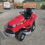Honda HF2417HME ride-on lawn tractor with red body, black seat, and large rear grass collector, designed for high-performance garden mowing.