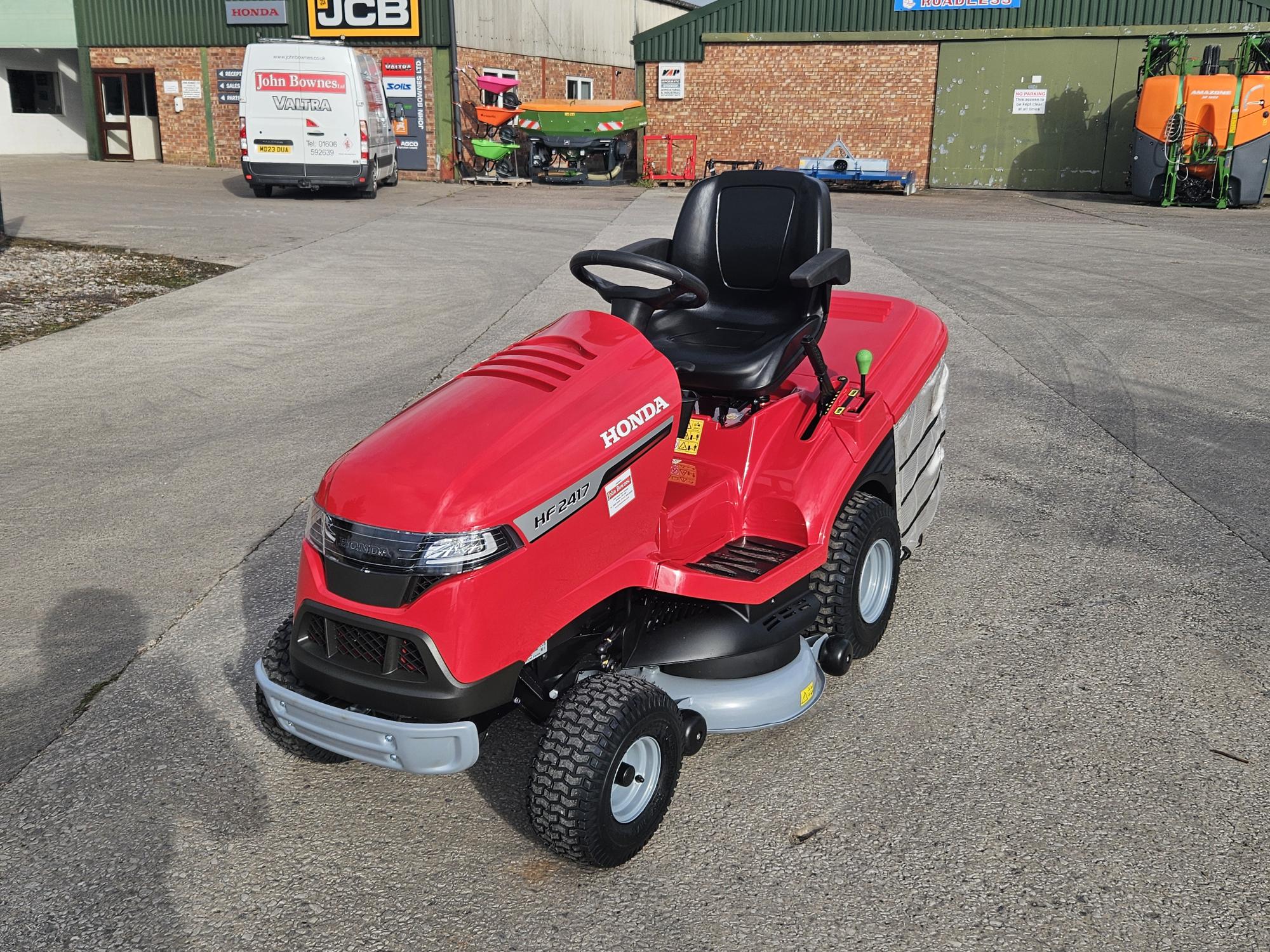 Honda HF2417HME ride-on lawn tractor with red body, black seat, and large rear grass collector, designed for high-performance garden mowing.